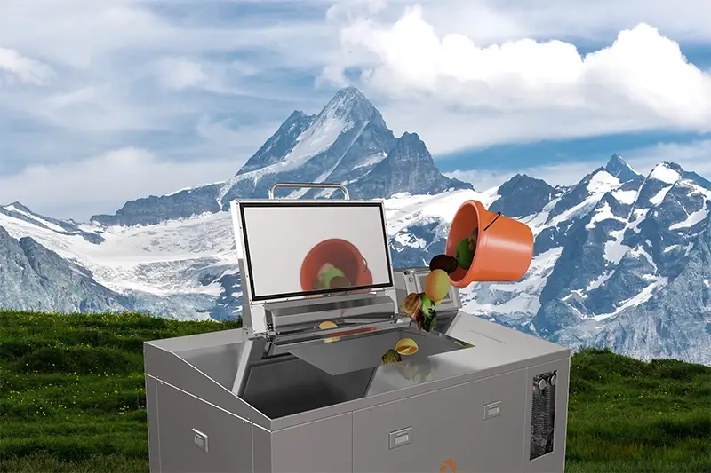 Power Knot LFC biodigester with its lid open receiving food scraps from an orange bucket, set against a dramatic Swiss Alpine mountain landscape with snow-capped peaks and green meadows.