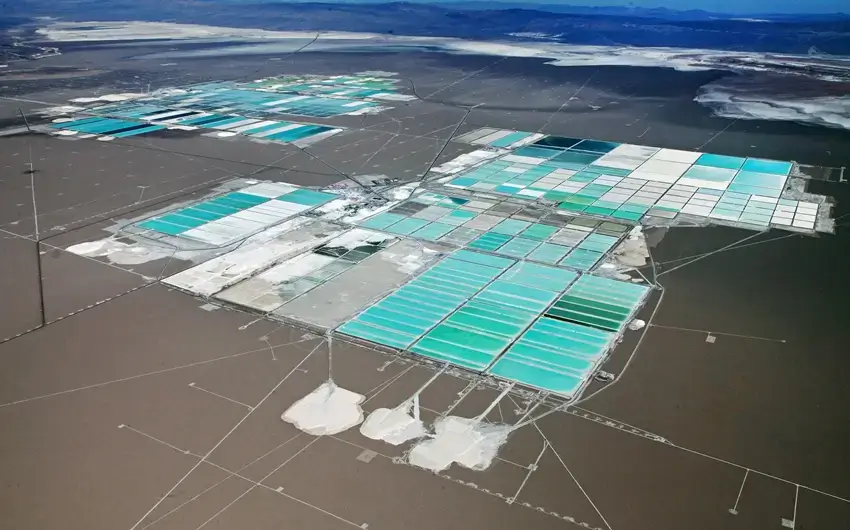 High-altitude aerial view of SQM lithium brine evaporation ponds at Salar de Atacama, Chile, showing a vast grid of turquoise and white mineral extraction pools across the arid desert salt flat landscape.
